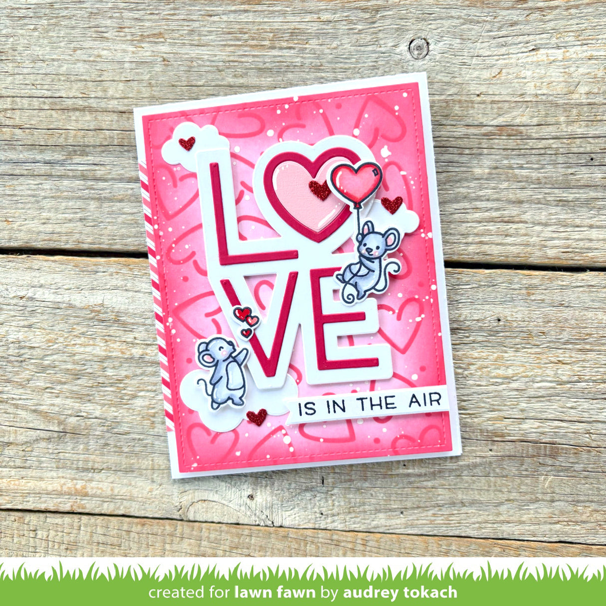 Pink card with 'LOVE IS IN THE AIR' text and cartoon mice on a wooden surface