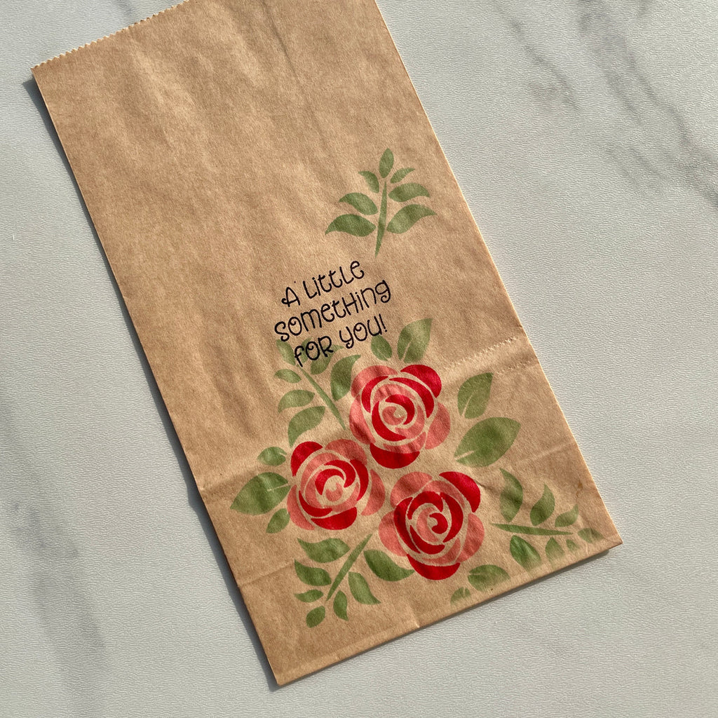 Kraft paper bag with red roses and 'A Little Something For You!' text on a marble surface