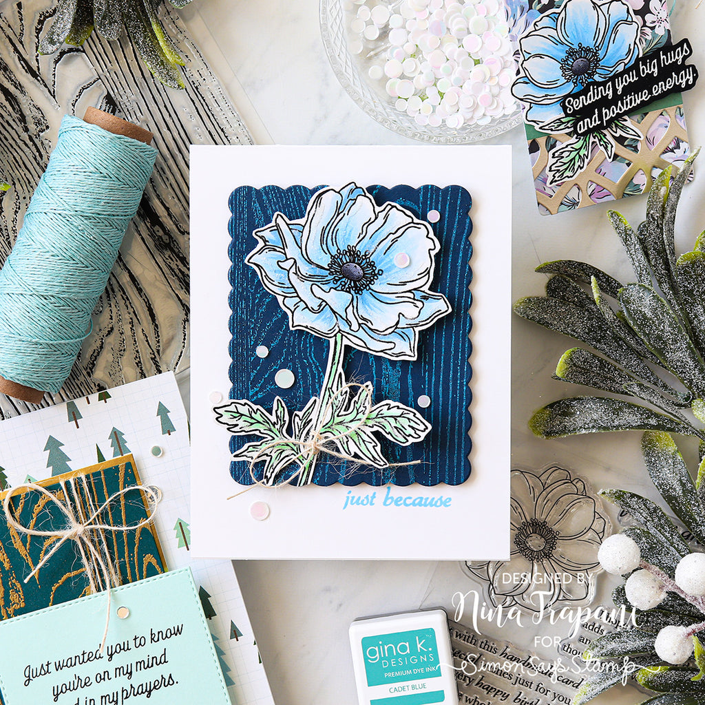 Card with blue flower design and text 'just because' surrounded by craft supplies.