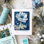 Card with blue flower design and text 'just because' surrounded by craft supplies.