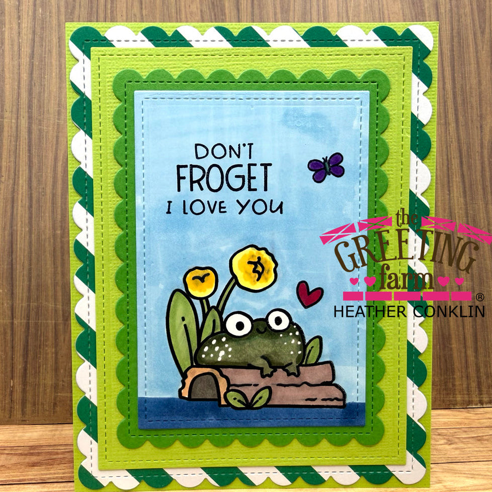 Greeting card with a frog illustration and text 'Don't Froget I Love You' on a wooden surface.