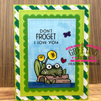 Greeting card with a frog illustration and text 'Don't Froget I Love You' on a wooden surface.