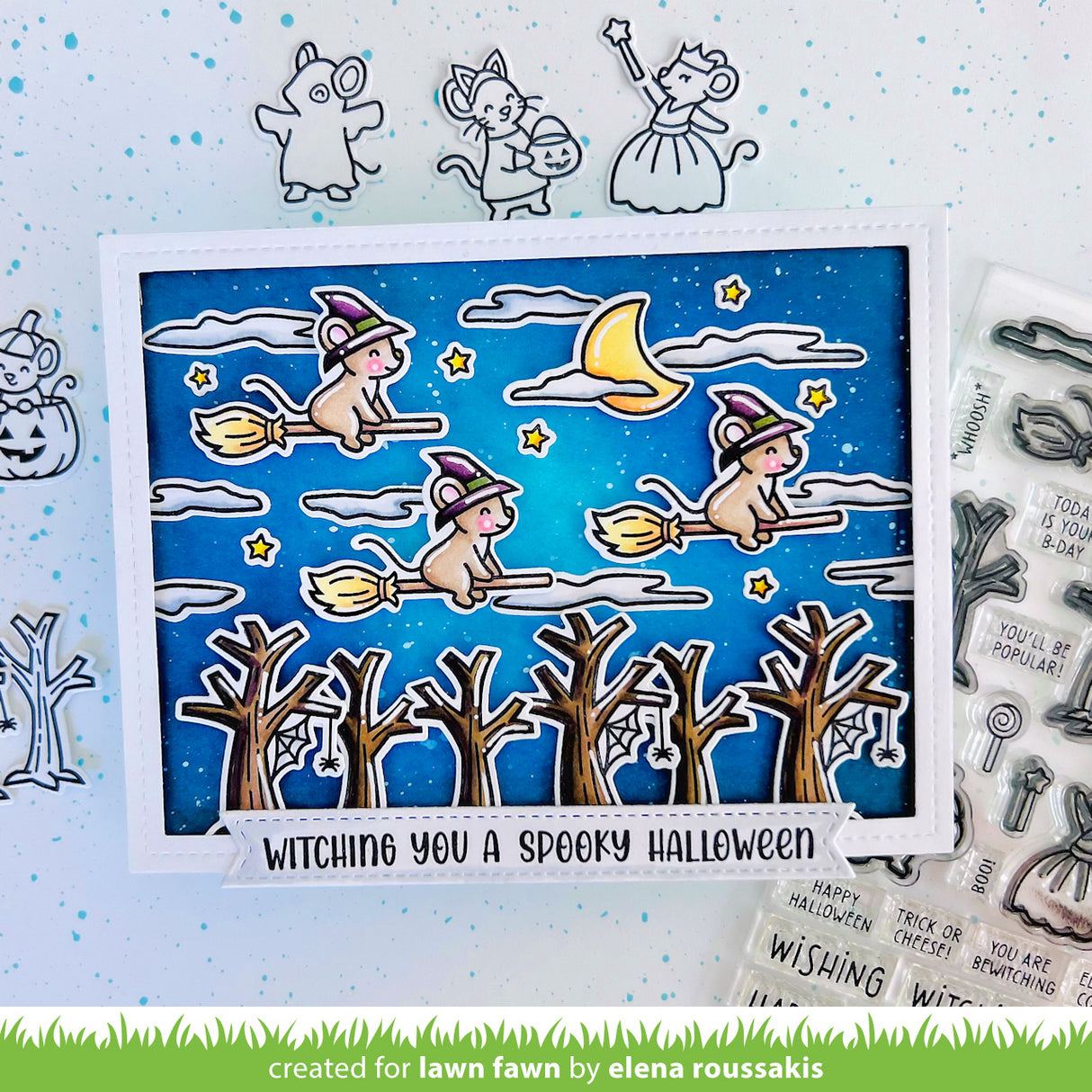 Halloween-themed card with cartoon cats on brooms, surrounded by Halloween-themed stamps and dies.