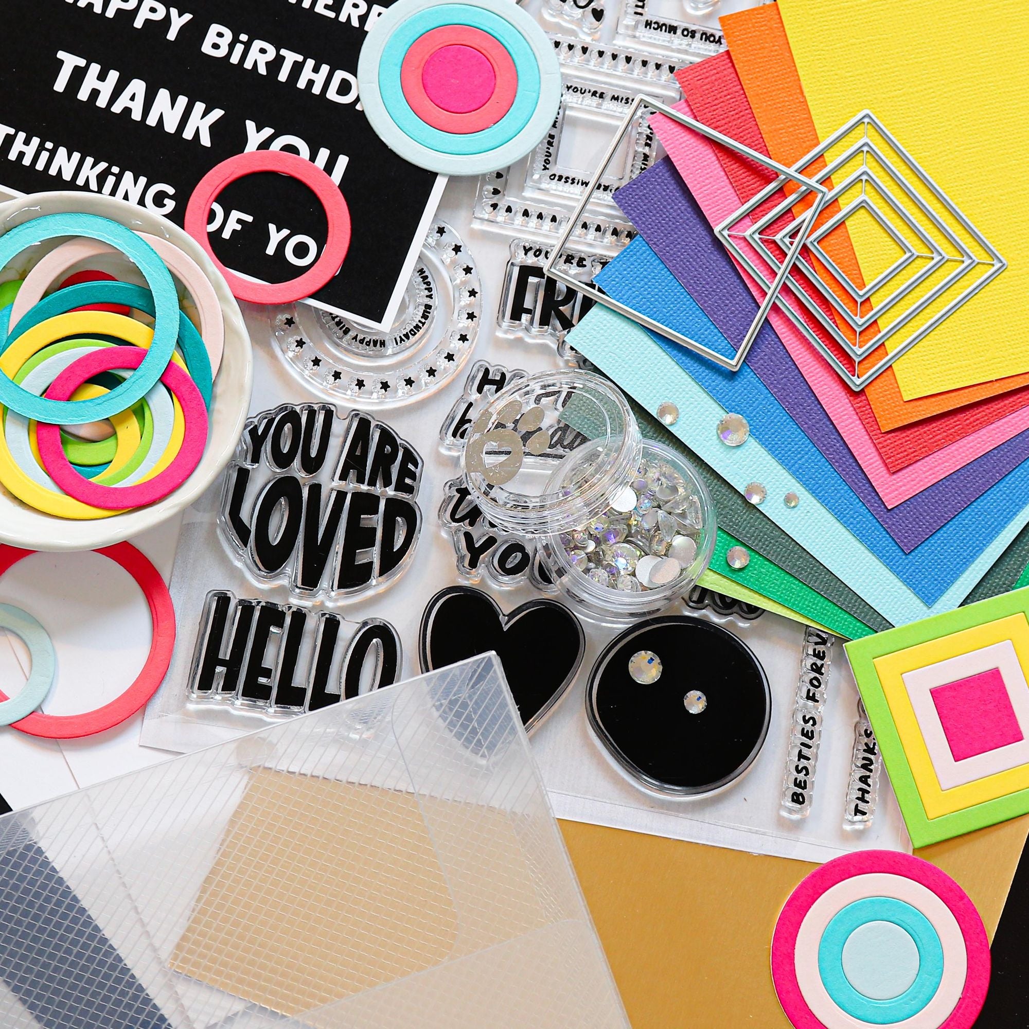 Collection of colorful craft supplies including paper, stickers, and decorative elements on a white background.