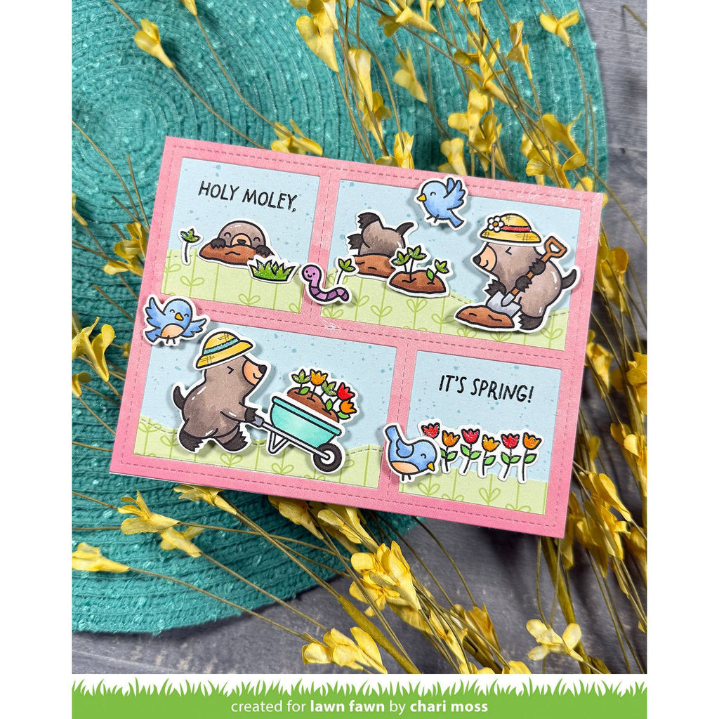 Card with moles in comic look and text on a pink border, surrounded by yellow flowers and green leaves.