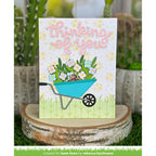 Card with 'thinking of you' text, wheelbarrow with flowers, and bear, set against a blurred natural background.
