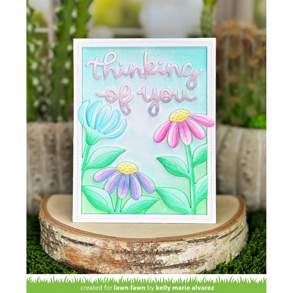 Card with flowers and 'thinking of you' text on a wooden stand with plants in the background