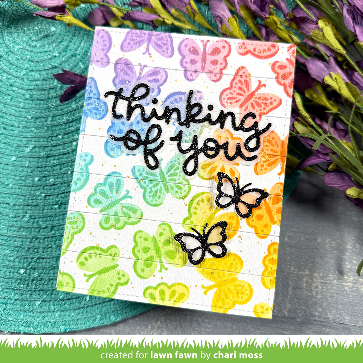 Card with colorful butterfly pattern and 'thinking of you' text, placed on a textured surface with flowers.