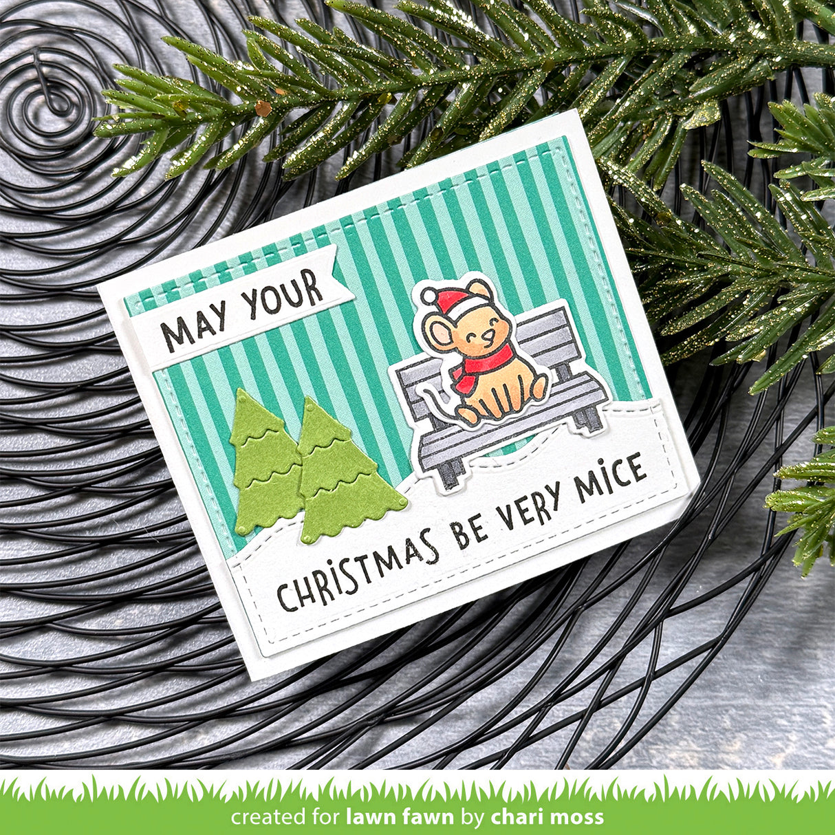 Christmas-themed card with a mouse on a bench and festive text, surrounded by greenery.