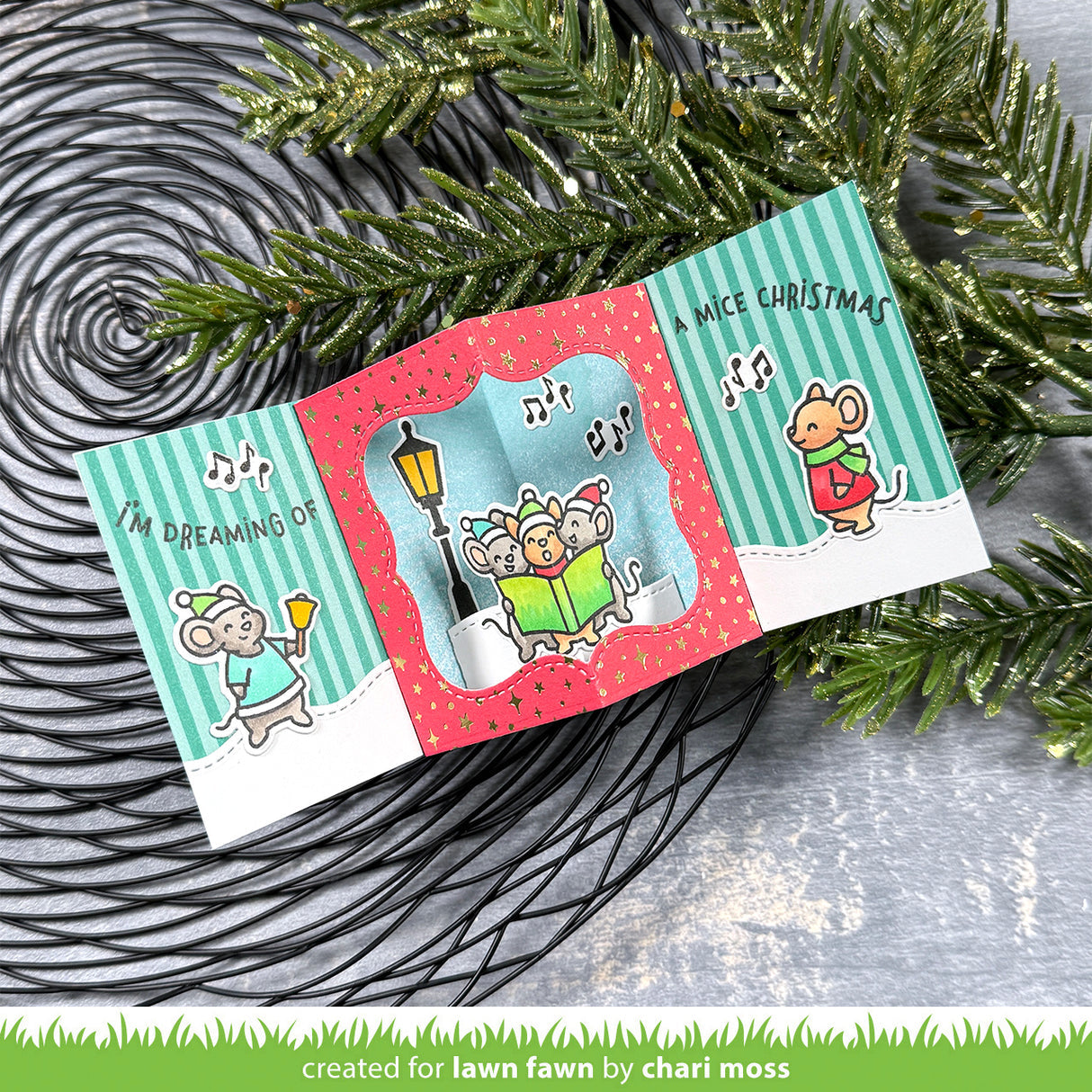 Christmas-themed card with cartoon mice and festive design, placed on a textured surface with greenery.