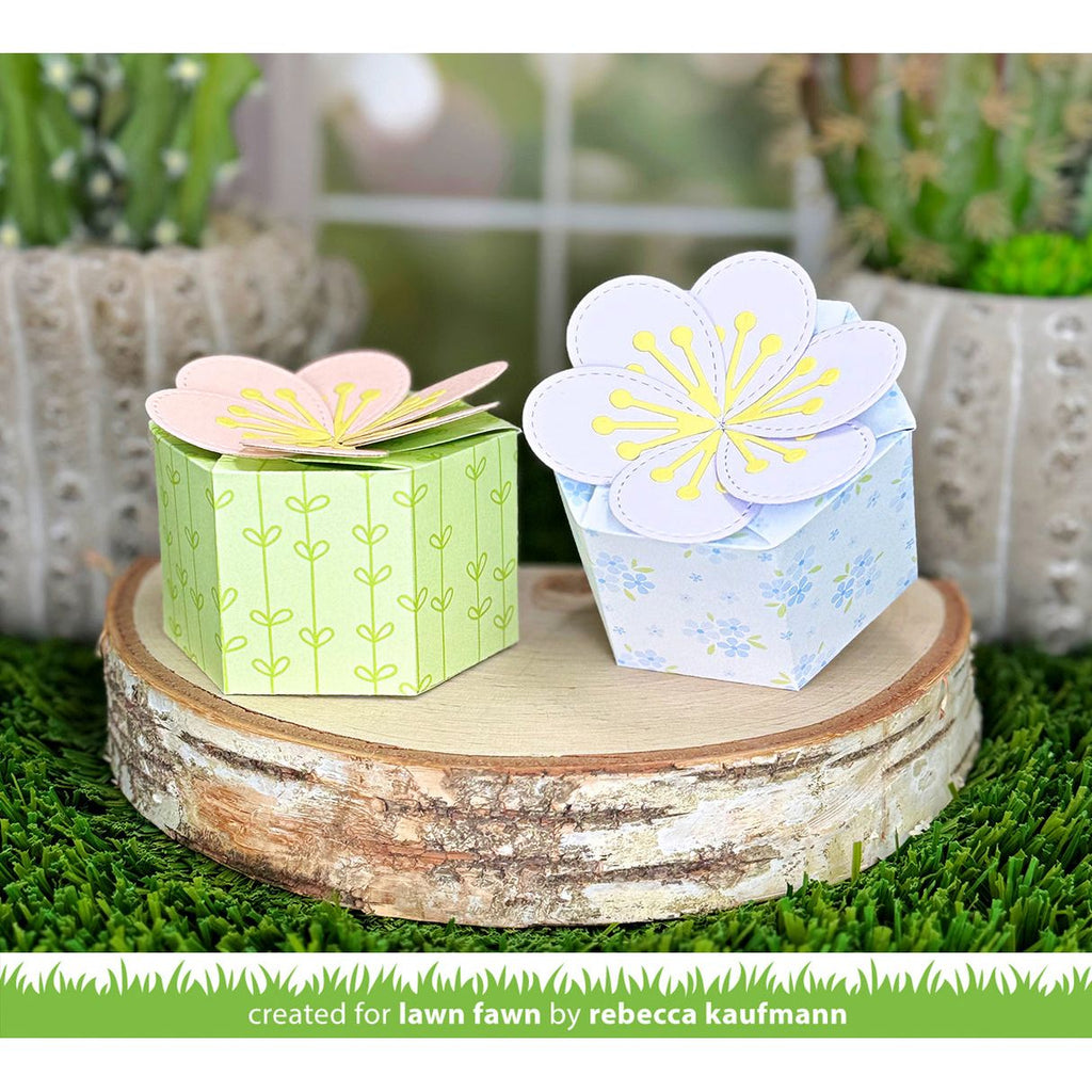 Two paper flower boxes on a wooden platform with plants in the background