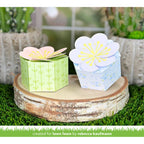 Two paper flower boxes on a wooden platform with plants in the background