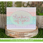 Greeting card with 'thinking of you' text on a decorative stand with plants in the background