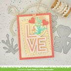 Card with 'LOVE' cutout and decorative elements on a textured surface with crafting tools.