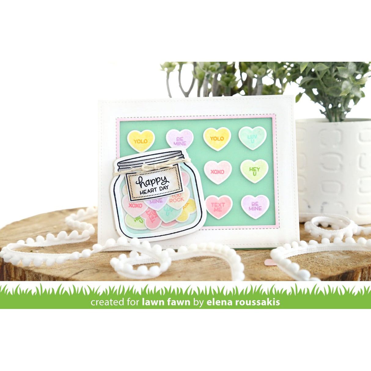 Card with a jar of candy hearts and 'Happy Heart Day' text, placed on a white surface with decorative elements.
