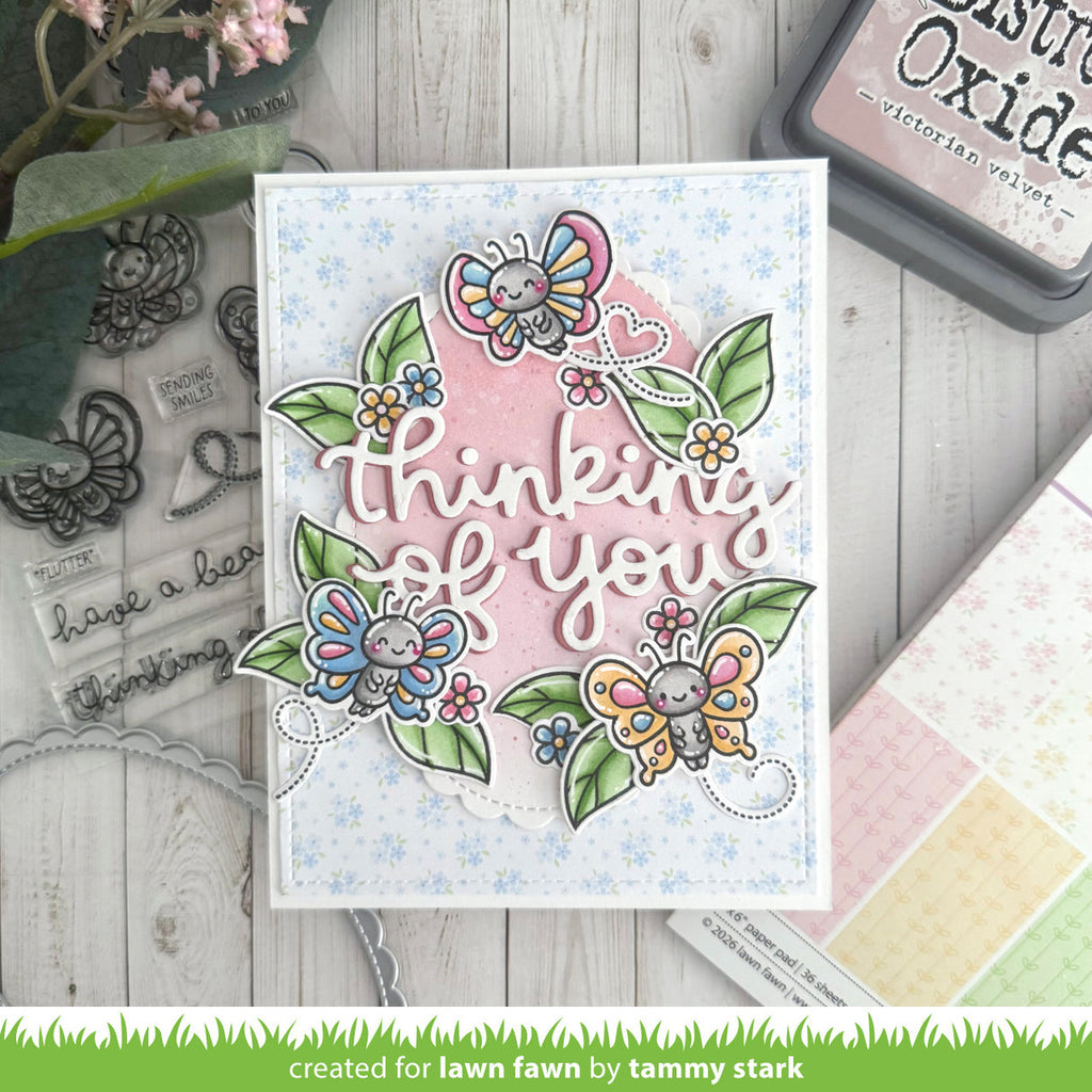 Card with butterfly design and 'thinking of you' text, surrounded by craft supplies on a wooden surface.