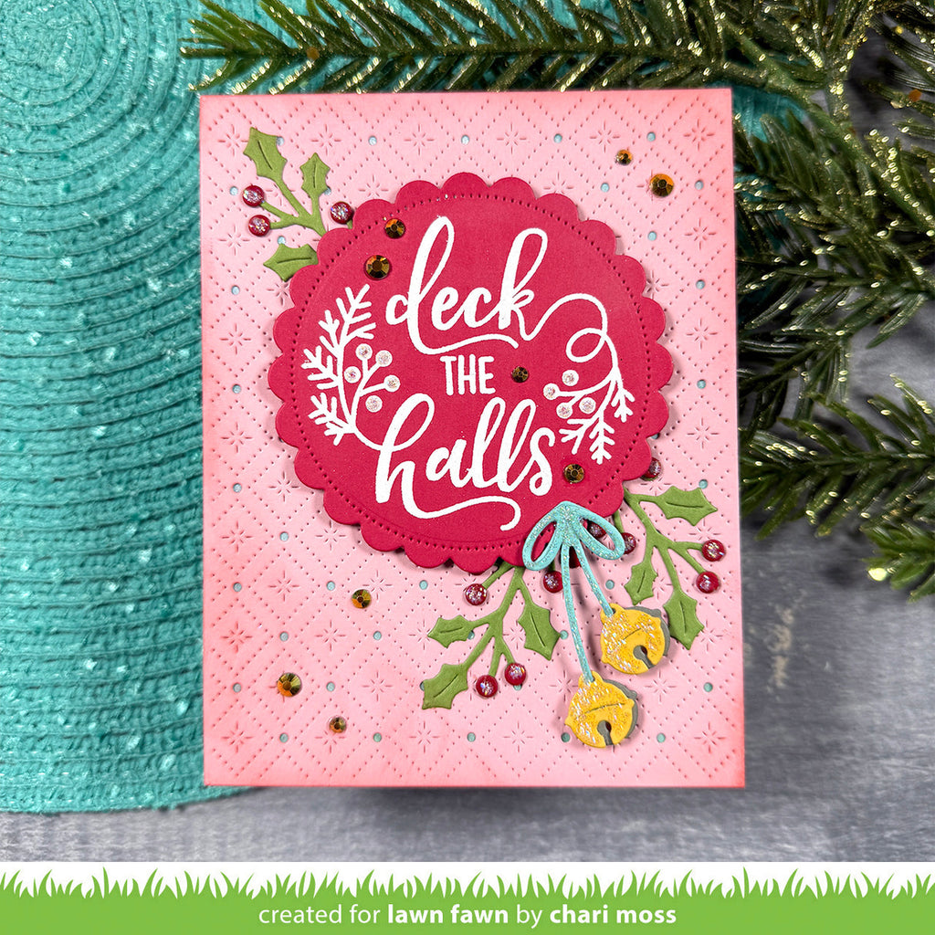 Pink Christmas card with 'deck the halls' text and holly decorations, surrounded by greenery.