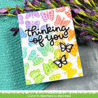 Card with colorful butterflies and 'thinking of you' text, placed on a textured surface with flowers.