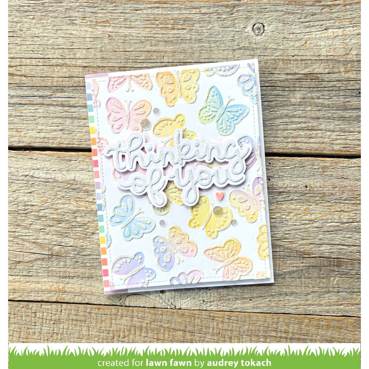 Card with colorful butterflies and 'thinking of you' text on a wooden surface, created for Lawn Fawn by Audrey Tokach.