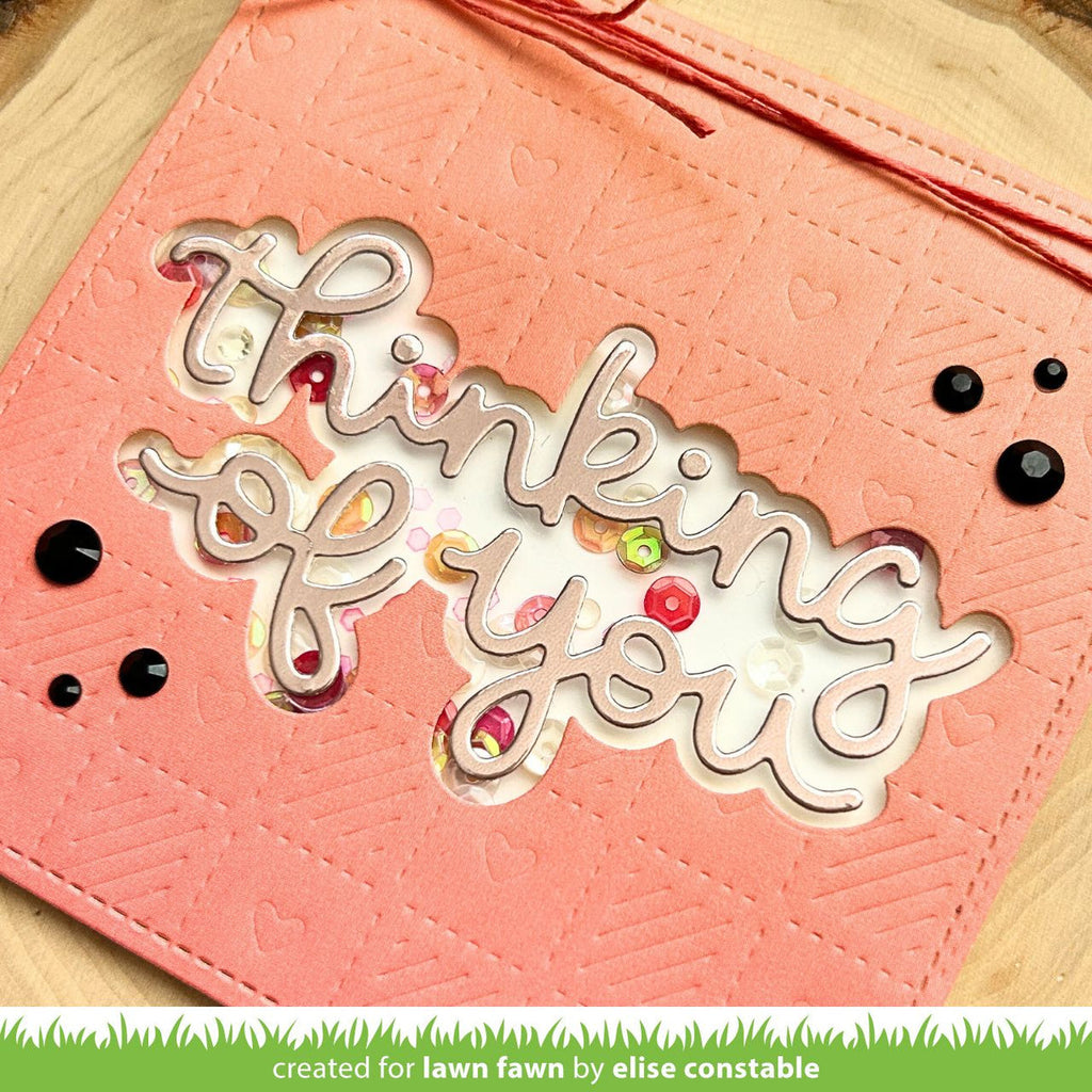 Coral card with 'thinking of you' text and decorative elements on a wooden surface.