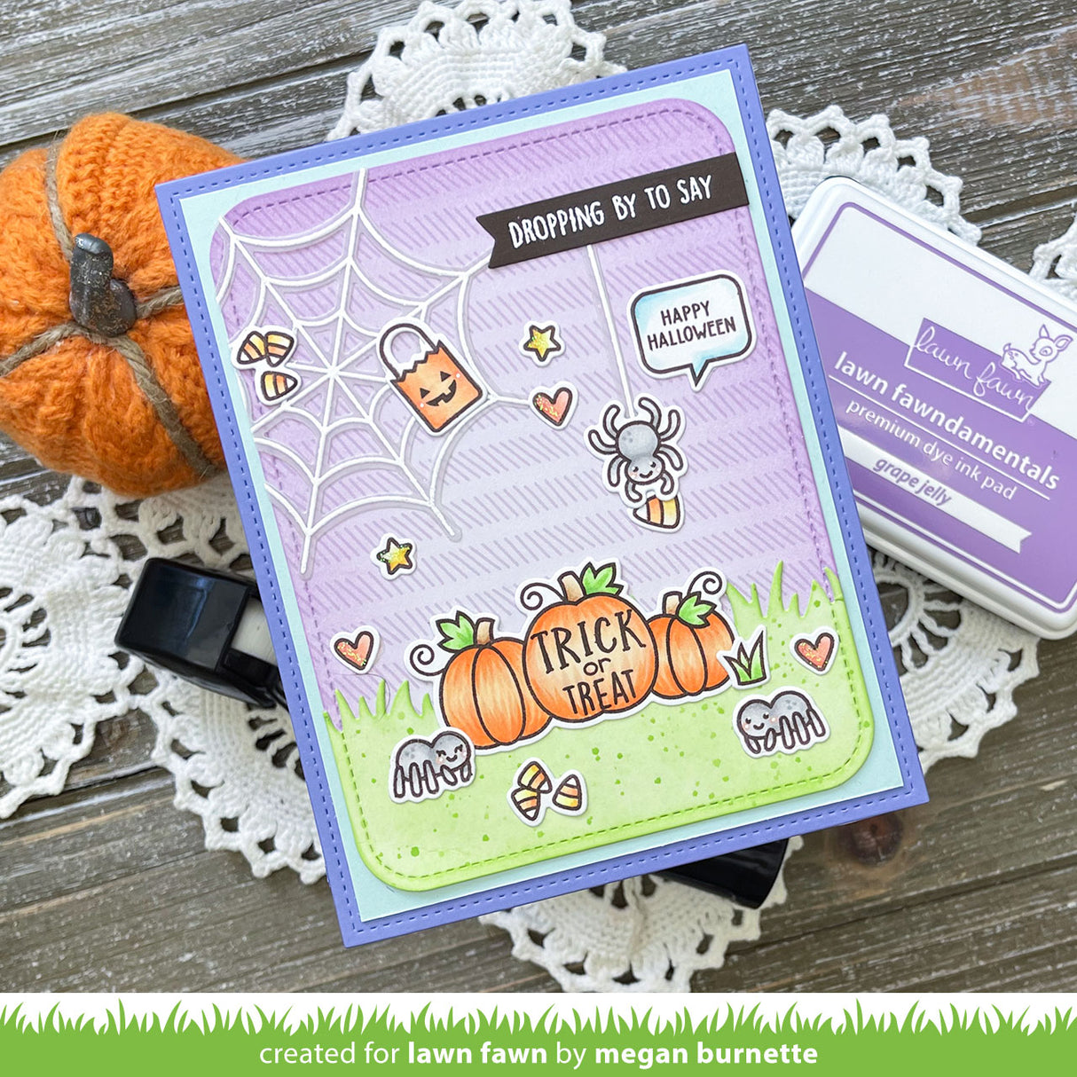 Halloween-themed card with pumpkins and spider on a wooden surface with a pumpkin and doily.