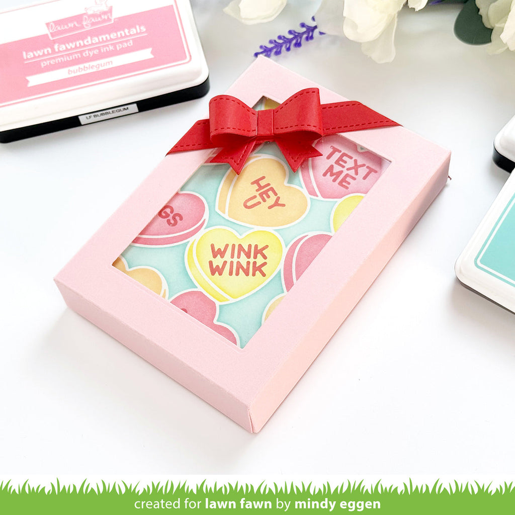 Pink box with a red ribbon containing colorful heart-shaped cards on a white background.