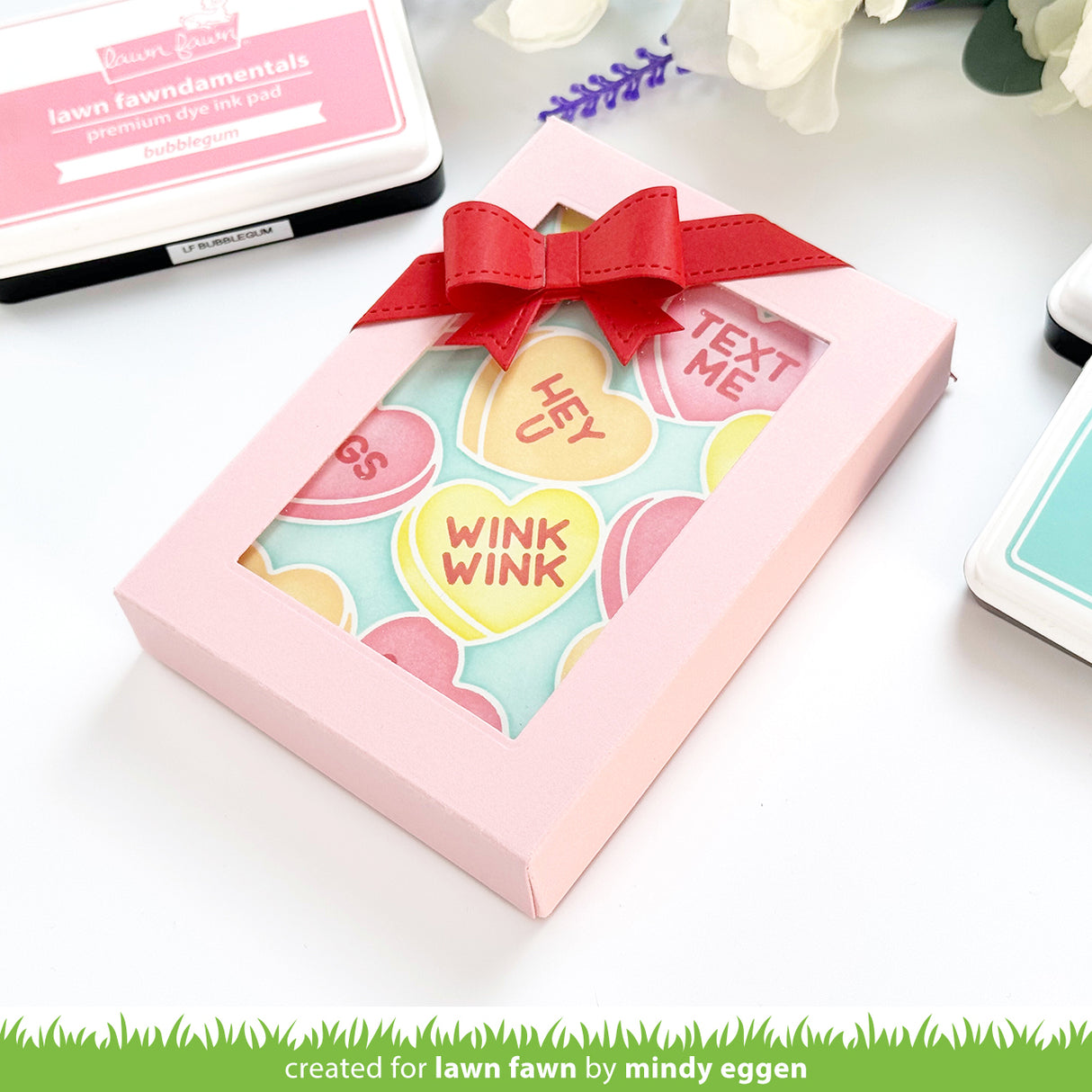Pink box with a red ribbon containing colorful heart-shaped cards on a white background.