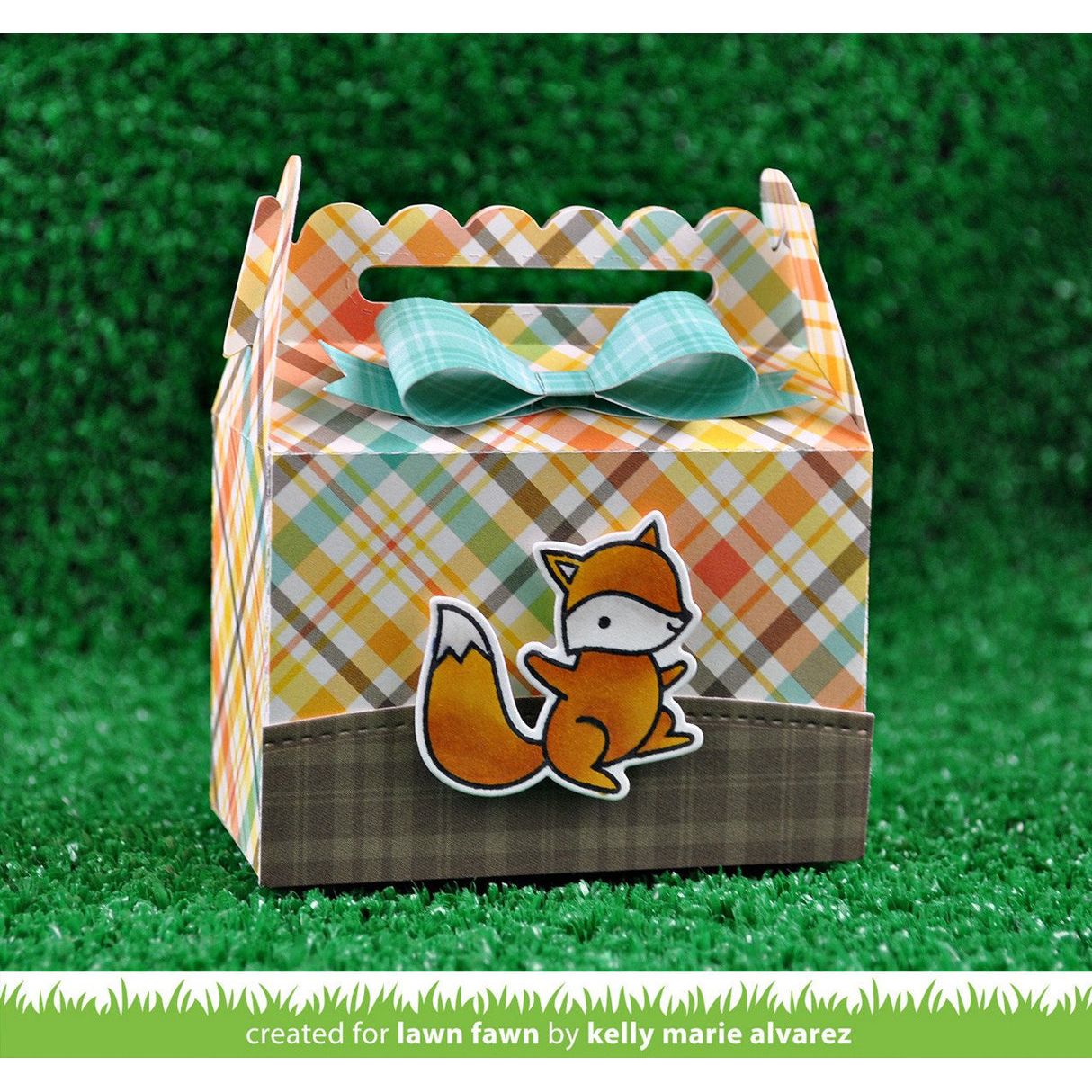 Decorative gift box with plaid pattern and fox design on a grassy background