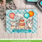 Card with ducks and birthday cake design on a checkered background, surrounded by stamping tools.