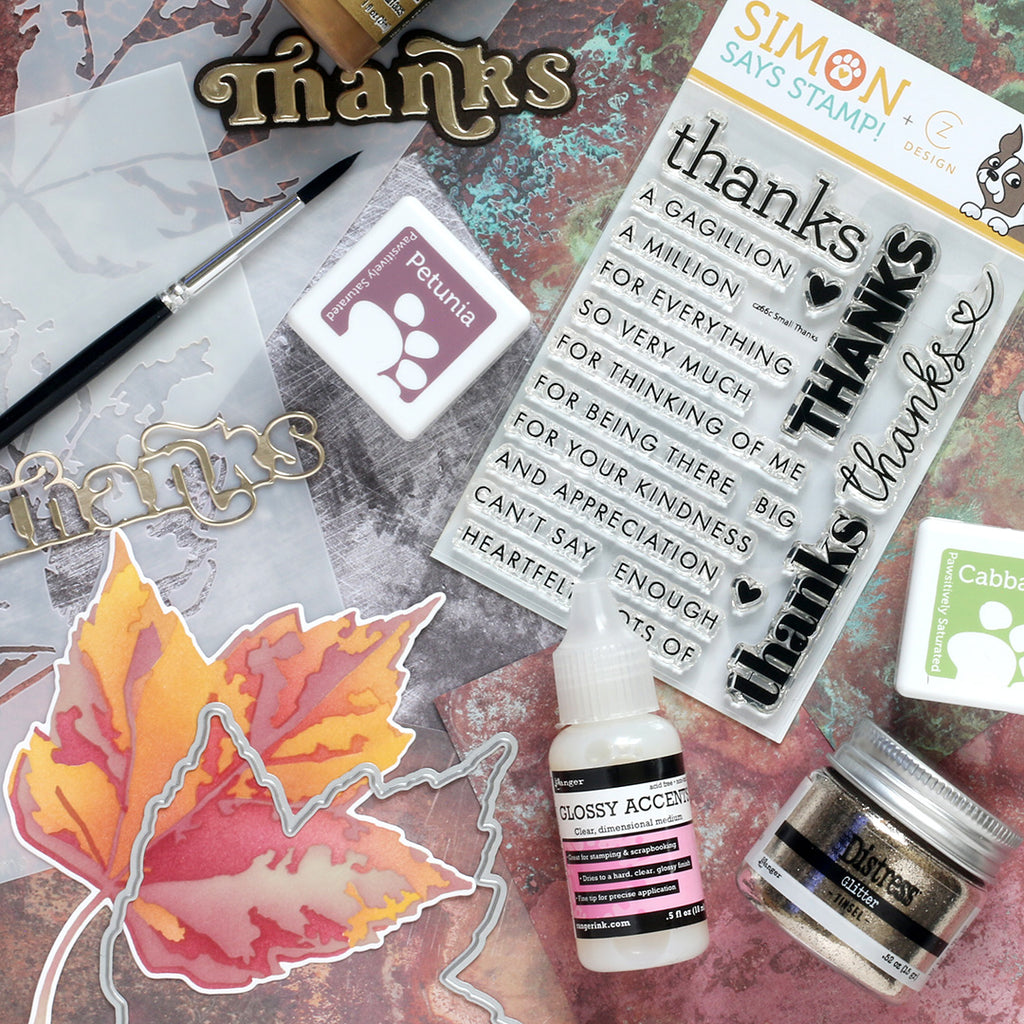 Stamp set with 'thanks' text, ink pad, leaf stamp, and glossy accents bottle on a textured surface.