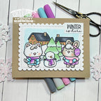 Card with winter-themed illustration of animals and snowman, surrounded by markers and scissors on a wooden surface. | color-code:ALT01