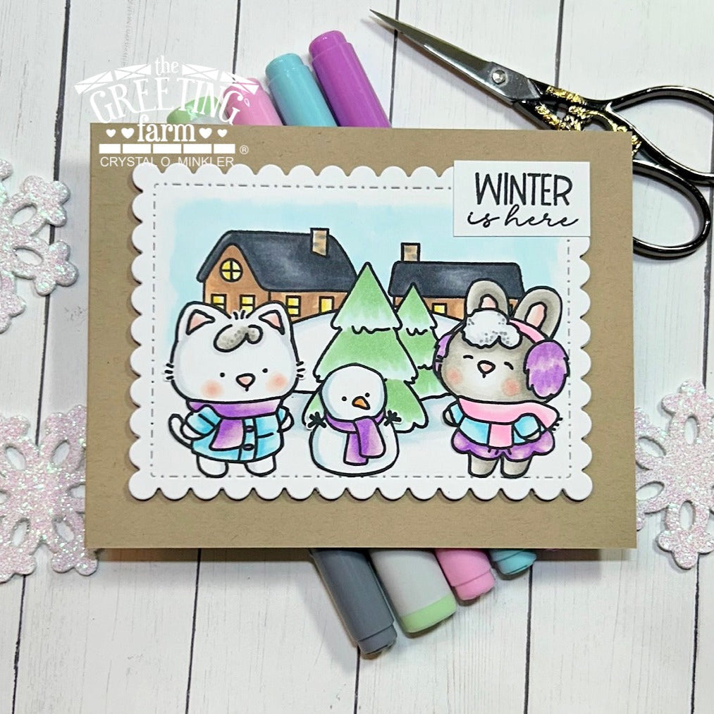 Card with winter-themed illustration of animals and snowman, surrounded by markers and scissors on a wooden surface. | color-code:ALT01