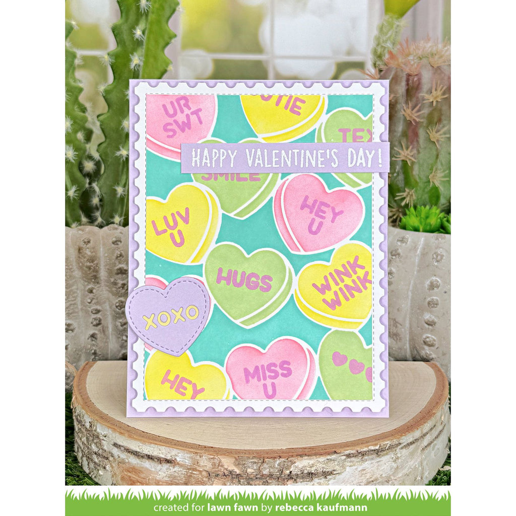 Valentine's Day card with colorful candy heart designs and 'Happy Valentine's Day!' text, placed on a wooden block with cacti in the background.